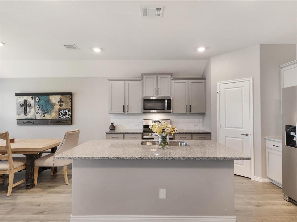 3257 Trails End Road Aubrey, TX 76227 - Photo 3 of 37 a kitchen with stainless steel appliances granite countertop a stove a sink a refrigerator and white cabinets with wooden floor