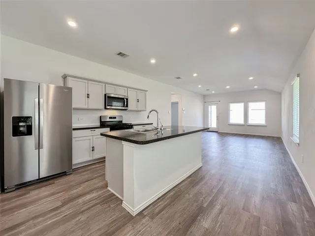 a kitchen with granite countertop a refrigerator a sink dishwasher a stove and white countertops with wooden floor