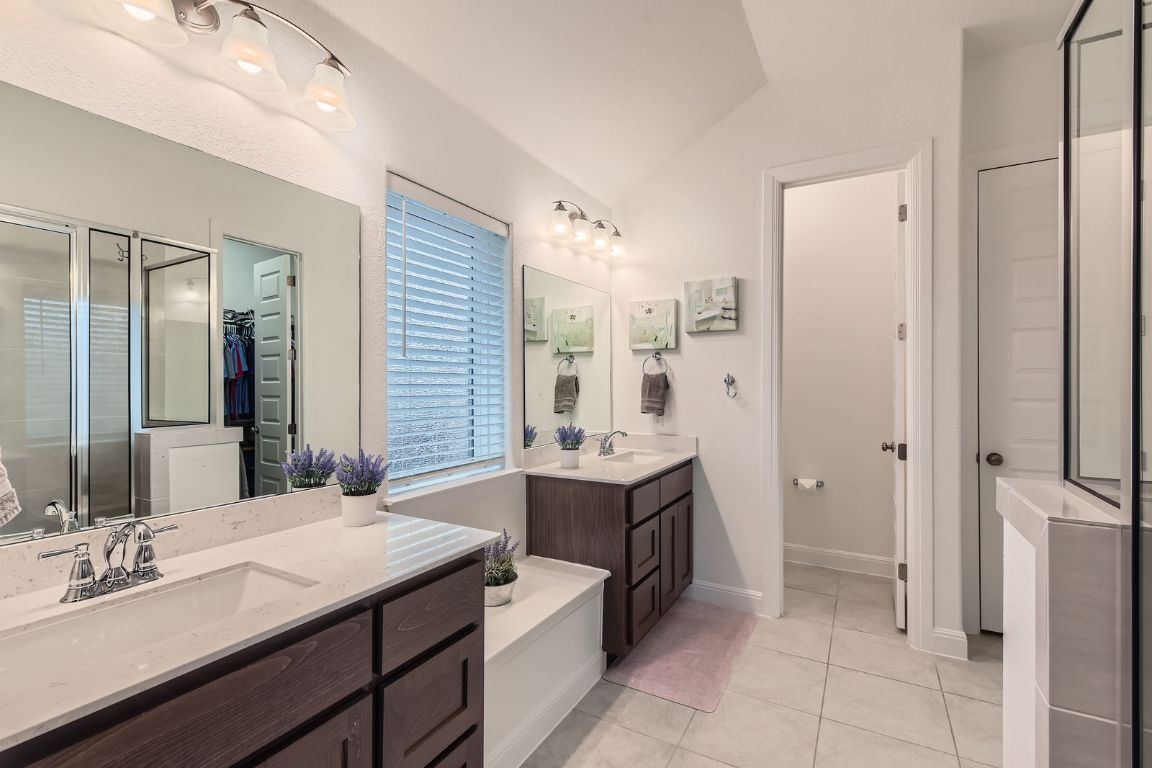 1332 Modoc Way Kyle, TX 78640 - Photo 16 of 28 Bathroom with two vanities, a shower stall, lofted ceiling, tile patterned floors, and a walk in closet