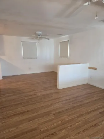 a view of an empty room with wooden floor and a ceiling fan