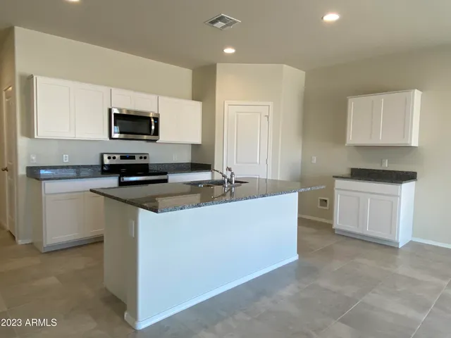 a kitchen with stainless steel appliances a sink a stove a microwave a refrigerator a sink and white cabinets