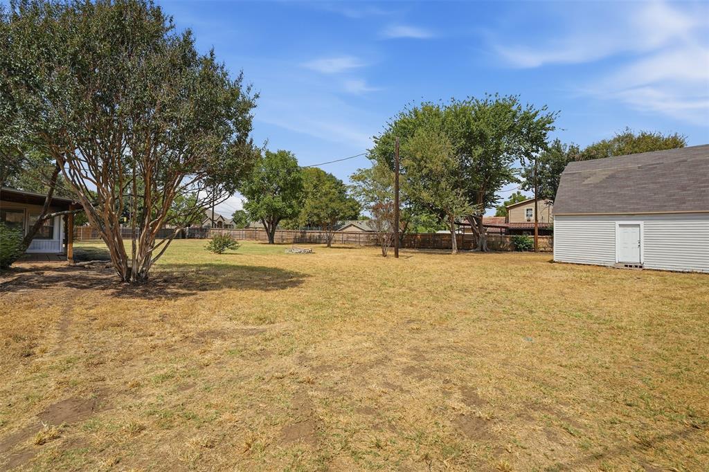 6880 Sandy Beach Road Azle, TX 76020 - Photo 26 of 32 Expansive backyard featuring mature trees, a detached storage building with a shingled roof, and a privacy fence