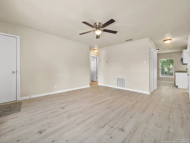 a view of an empty room with wooden floor and a ceiling fan