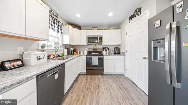 a kitchen with stainless steel appliances granite countertop a refrigerator a stove top oven a sink and dishwasher with wooden floor