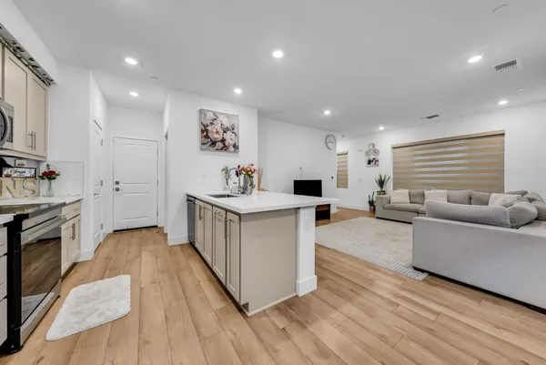 a large white kitchen with stainless steel appliances granite countertop a large counter top a couch and a view of living room