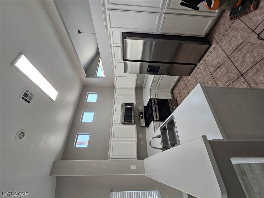 1418 Reebok Terrace Henderson, NV 89014 - Photo 4 of 39 A well-lit kitchen with sleek white cabinetry, stainless steel appliances, and a vaulted ceiling creates an inviting atmosphere.