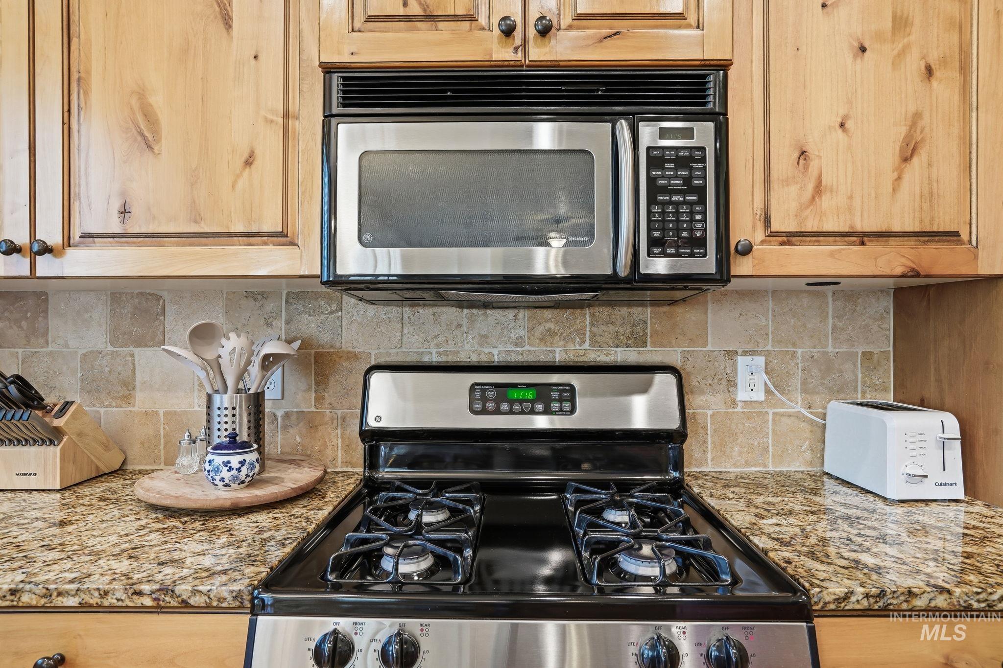 3969 North Hollymount Way Meridian, ID 83646 - Photo 13 of 47 Kitchen featuring stainless steel appliances, a gas range with an overhead microwave, granite countertops, a tiled backsplash, and wood cabinetry