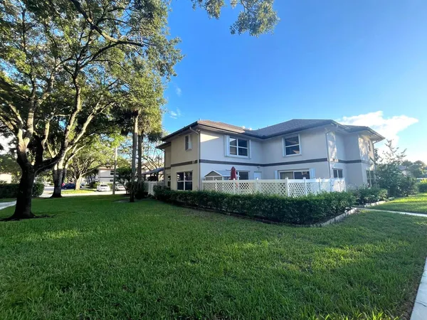 a view of a white house next to a yard with big trees