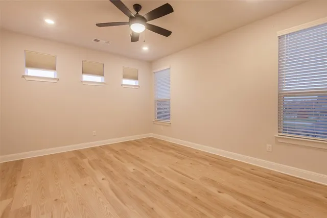 an empty room with wooden floor fan and windows