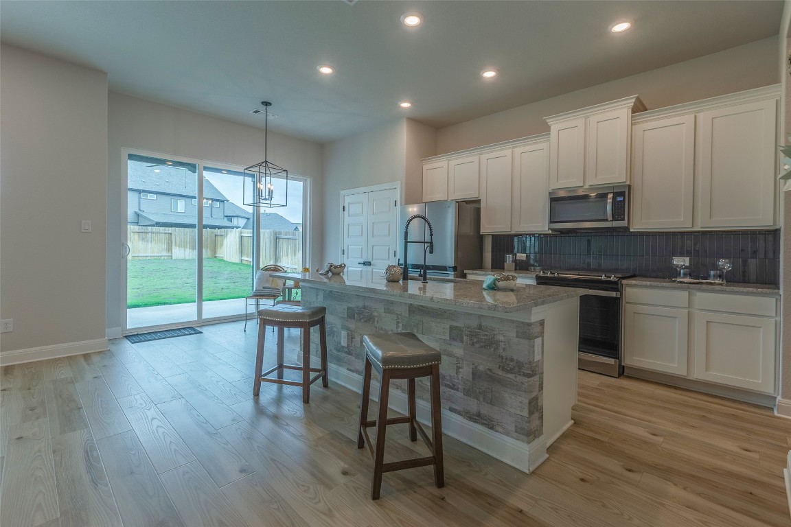 103 Periwinkle Lane Bastrop, TX 78602 - Photo 4 of 35 a kitchen with kitchen island granite countertop a stove a sink a refrigerator and white cabinets with wooden floor