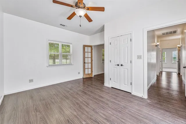 an empty room with wooden floor chandelier fan and windows