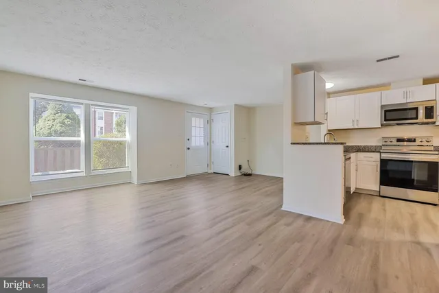 an empty room with wooden floor kitchen view and a window