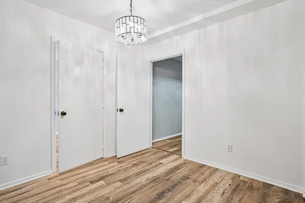 an empty room with a chandelier fan and wooden floor