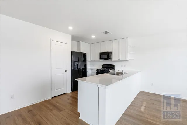 a kitchen with stainless steel appliances a refrigerator oven a sink with white cabinets and wooden floor