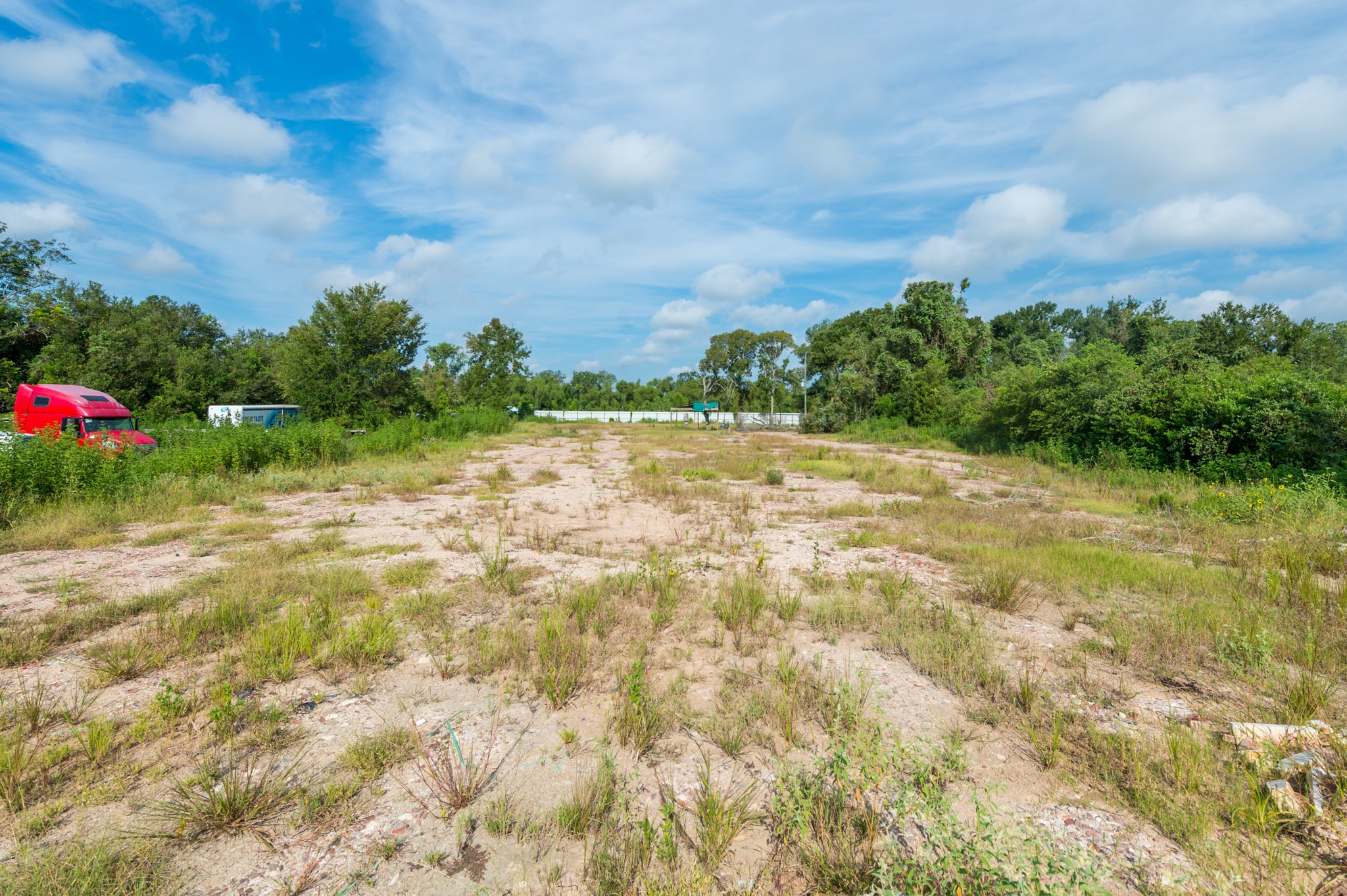 1353 Seidel Road Brookshire, TX 77423 - Photo 13 of 35 This photo shows a large, open plot of land with sparse vegetation and surrounding trees under a blue sky. Ideal for development or agriculture, it offers a spacious and natural setting.