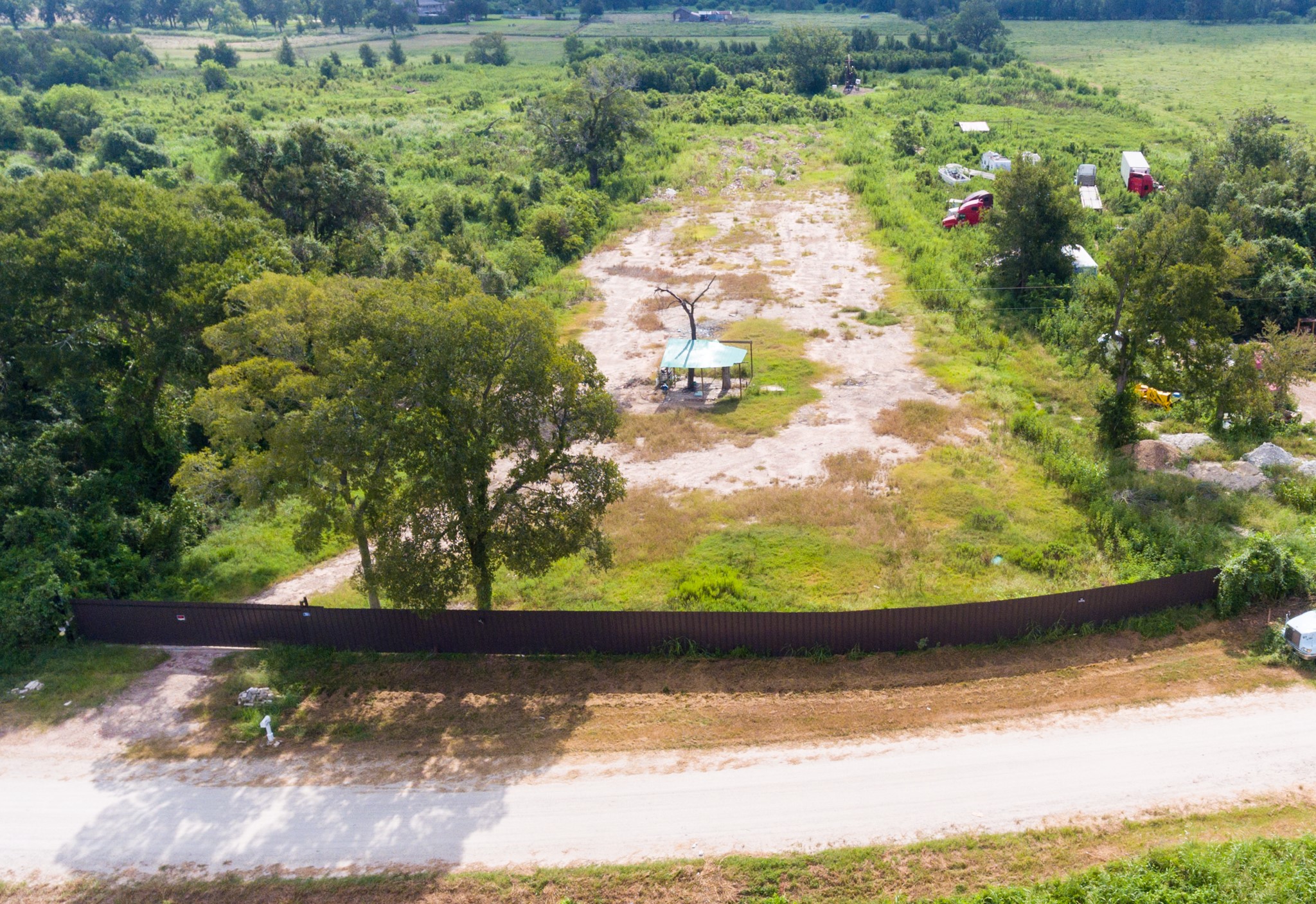 1353 Seidel Road Brookshire, TX 77423 - Photo 28 of 35 This photo shows a large, open plot of land surrounded by greenery, with a few scattered trees and a fence at the front. It's a secluded area, ideal for development, offering ample space and scenic views.