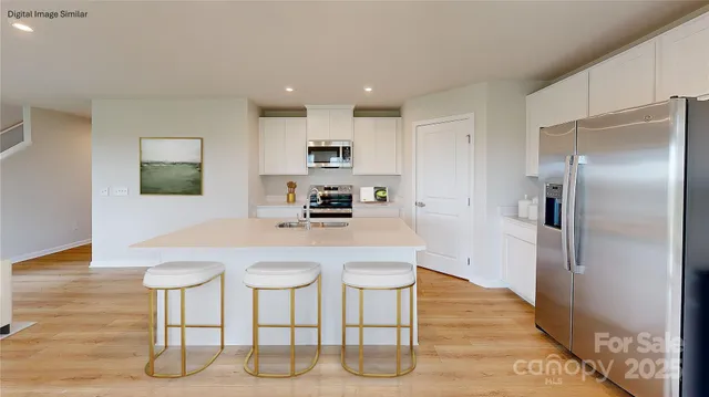 a kitchen with stainless steel appliances kitchen island granite countertop a refrigerator a stove a microwave oven with white cabinets and wooden floor