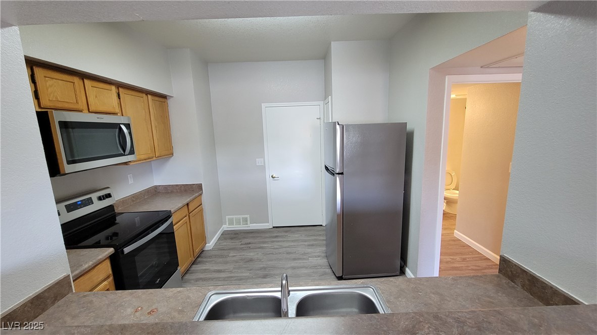 6650 West Warm Springs Road, Unit 1032 Las Vegas, NV 89118 - Photo 7 of 17 Kitchen featuring appliances with stainless steel finishes, light wood finished floors, and brown cabinets