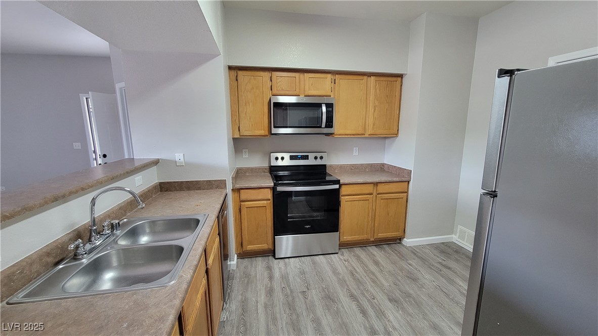 6650 West Warm Springs Road, Unit 1032 Las Vegas, NV 89118 - Photo 8 of 17 Kitchen featuring appliances with stainless steel finishes, light wood-style floors, light countertops, and brown cabinets