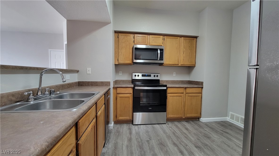 6650 West Warm Springs Road, Unit 1032 Las Vegas, NV 89118 - Photo 9 of 17 Kitchen featuring stainless steel appliances, light wood-style flooring, and brown cabinetry