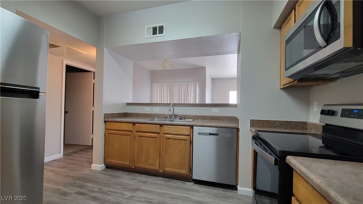 6650 West Warm Springs Road, Unit 1032 Las Vegas, NV 89118 - Photo 10 of 17 Kitchen featuring stainless steel appliances, brown cabinetry, and light wood finished floors