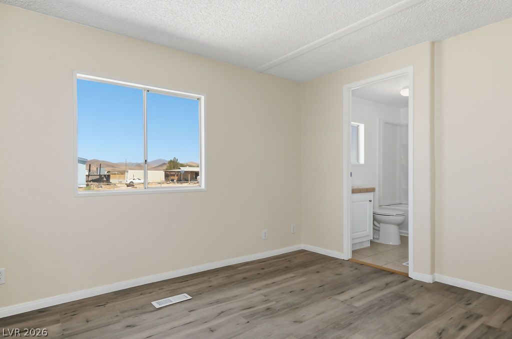 4550 Horn Road Pahrump, NV 89048 - Photo 11 of 20 A comfortable primary bedroom with light-toned walls, wood-look flooring, and a window offering views of distant mountains.