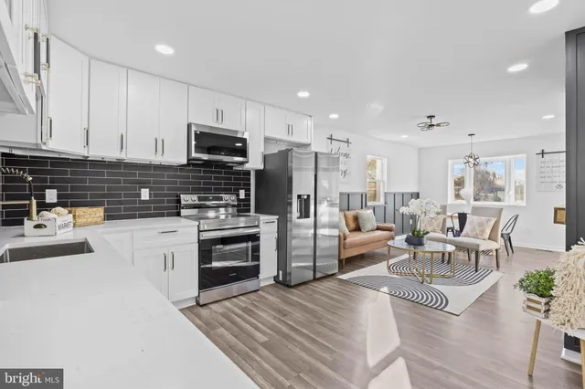 a kitchen with stainless steel appliances a stove a sink a refrigerator white cabinets and couches with wooden floor