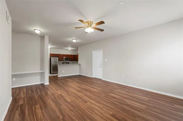a view of an empty room with wooden floor and a ceiling fan