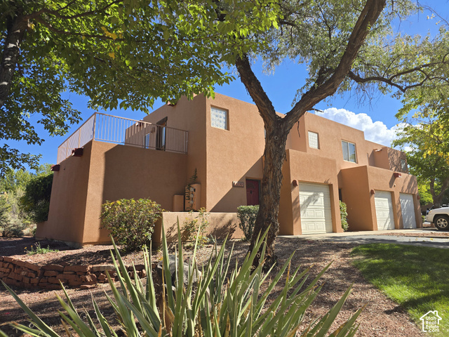 3299 Fairway Loop Moab, UT 84532 - Photo 1 of 23 Southwestern-style stucco exterior with multiple garage doors, an upper-level balcony with white railings, and mature trees
