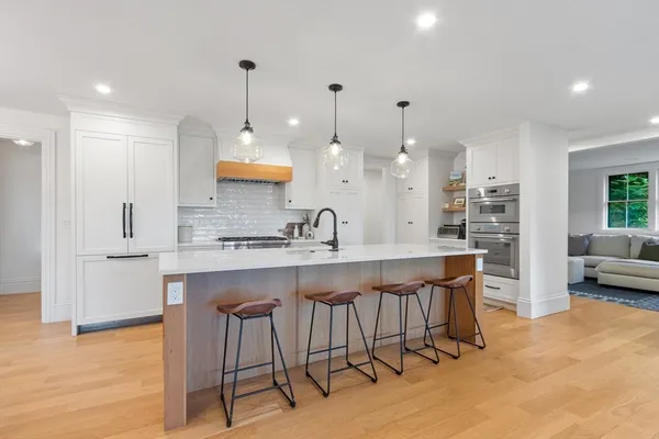 a large kitchen with kitchen island a island a sink a stove and a large refrigerator with wooden floor