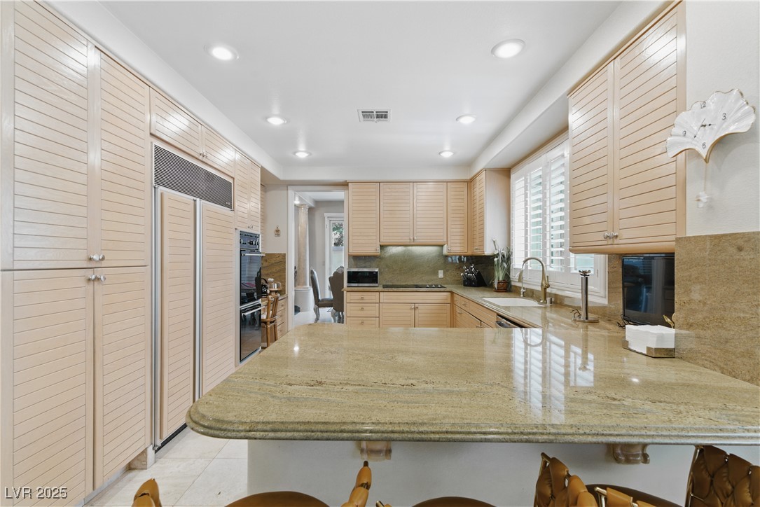 8215 Crow Valley Lane Las Vegas, NV 89113 - Photo 20 of 43 Kitchen featuring a peninsula, light stone counters, a kitchen breakfast bar, backsplash, and paneled fridge