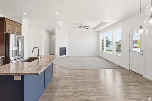 3636 West 910 South Syracuse, UT 84075 - Photo 32 of 70 Open-concept living space with wood-finish flooring, a kitchen island featuring a granite countertop and undermount sink, and a stainless steel refrigerator