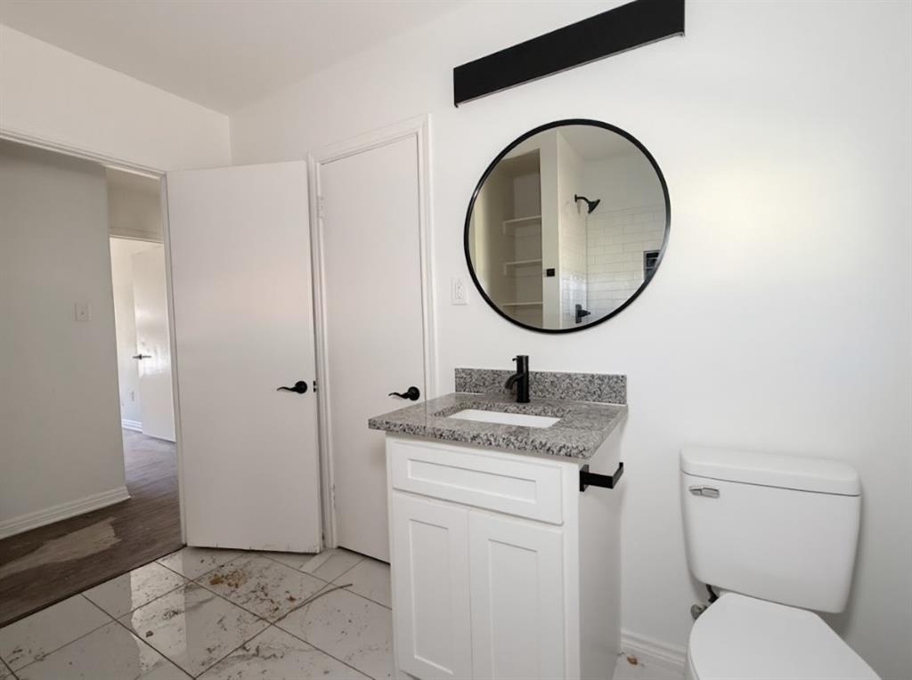 1512 West Day Street Denison, TX 75020 - Photo 10 of 14 a bathroom with a granite countertop toilet a sink and mirror