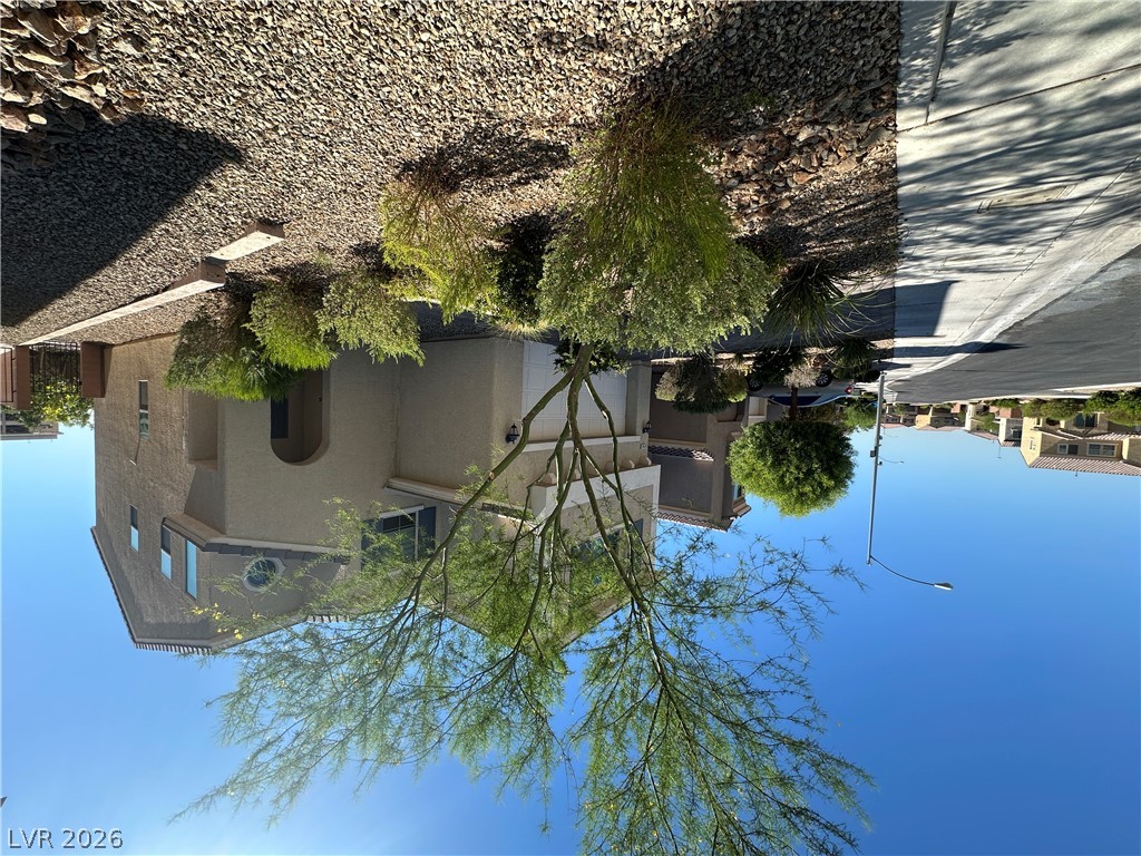 6784 Pivot Point Street Las Vegas, NV 89148 - Photo 2 of 27 A gracefully arching tree frames the desert-adapted landscaping and charming stucco facade of this residence.