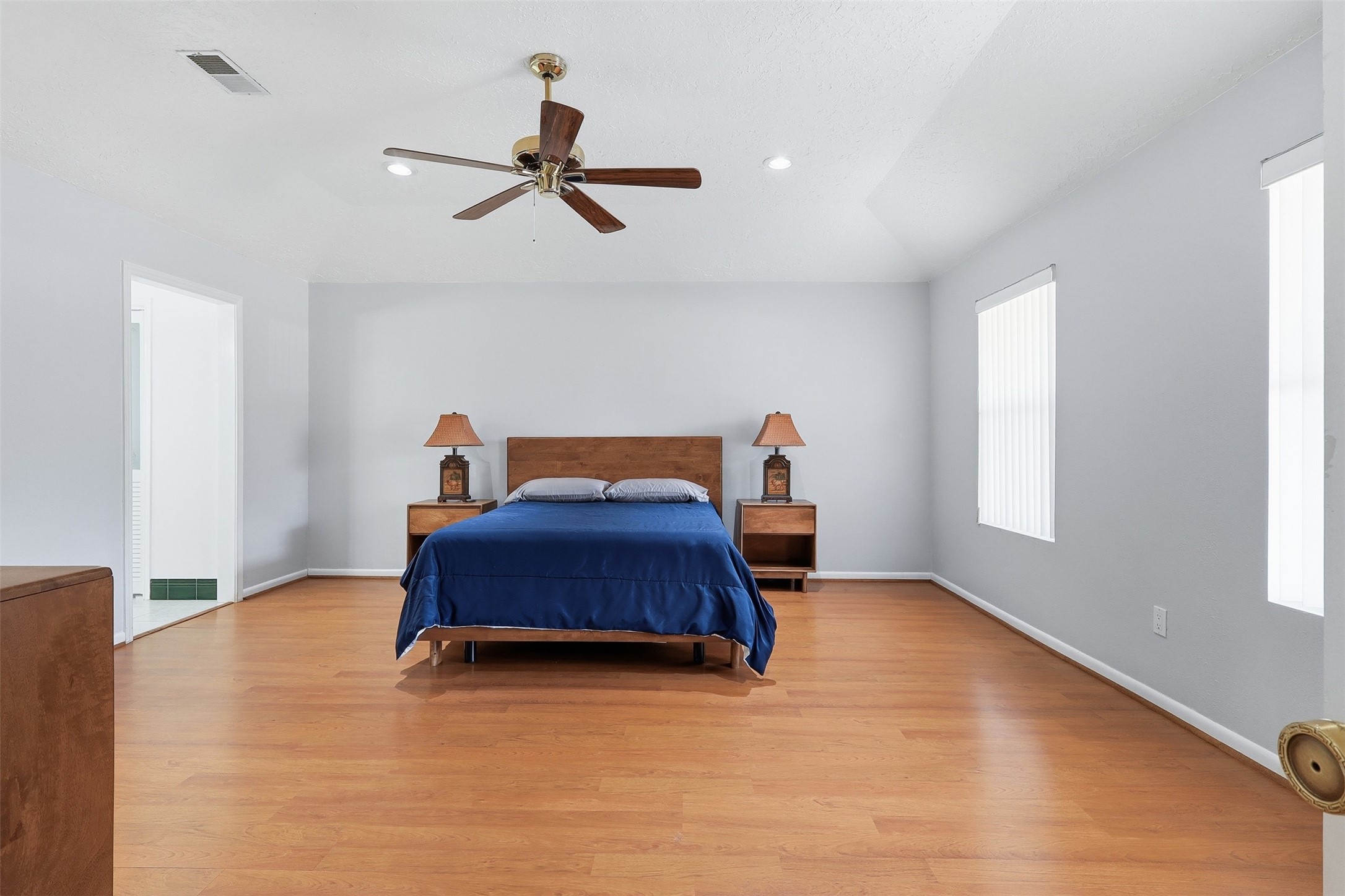 614 Tallow Drive Conroe, TX 77385 - Photo 19 of 36 Spacious bedroom with a vaulted ceiling, featuring hardwood floors and ample natural light. It includes a ceiling fan, a large bed with matching nightstands, and an ensuite bathroom. Neutral walls provide a modern look.