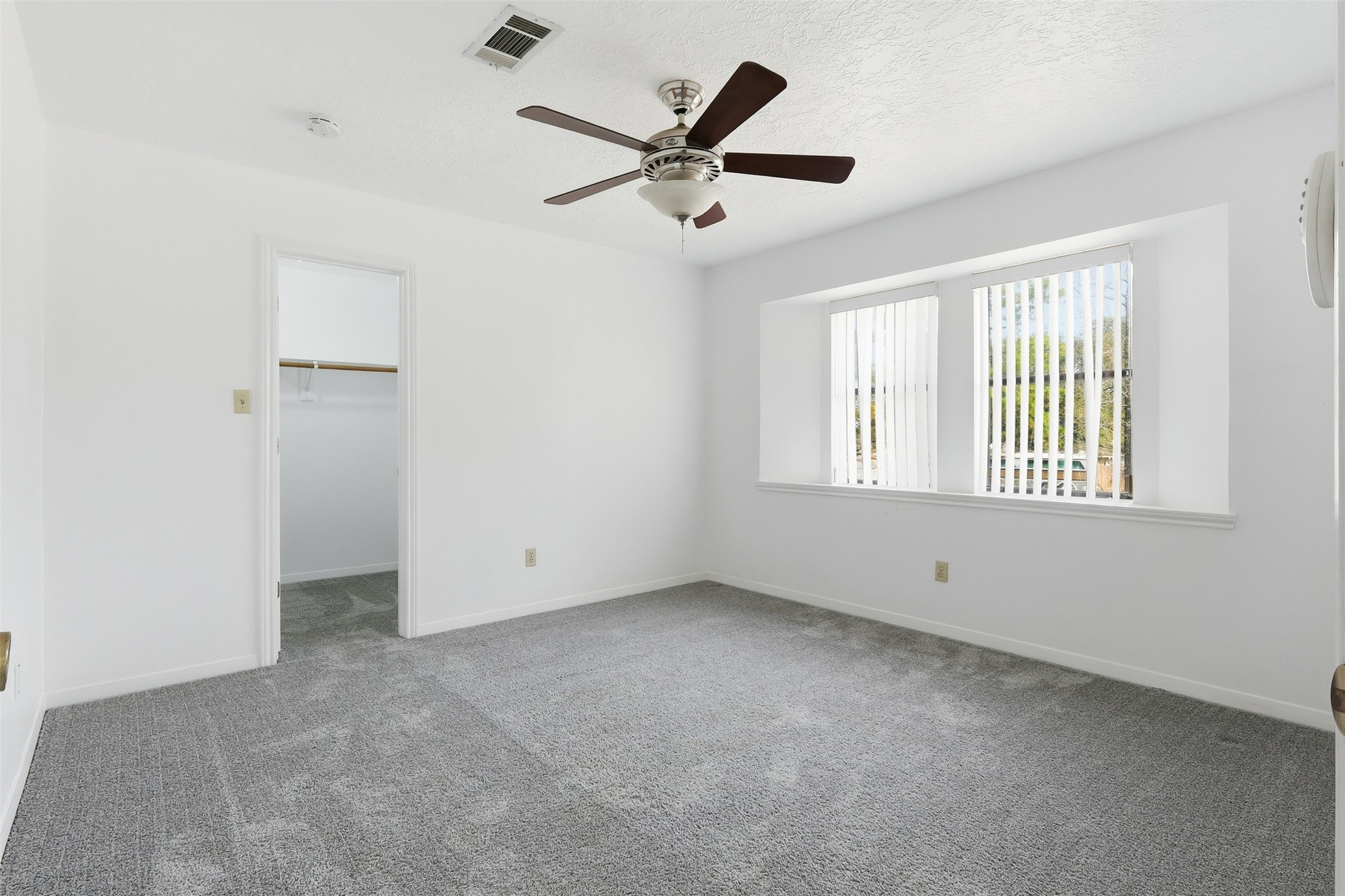 614 Tallow Drive Conroe, TX 77385 - Photo 25 of 36 Upstairs Bedroom with neutral walls and carpet, featuring a ceiling fan and a large window with vertical blinds. It includes an attached walk-in closet for convenient storage.