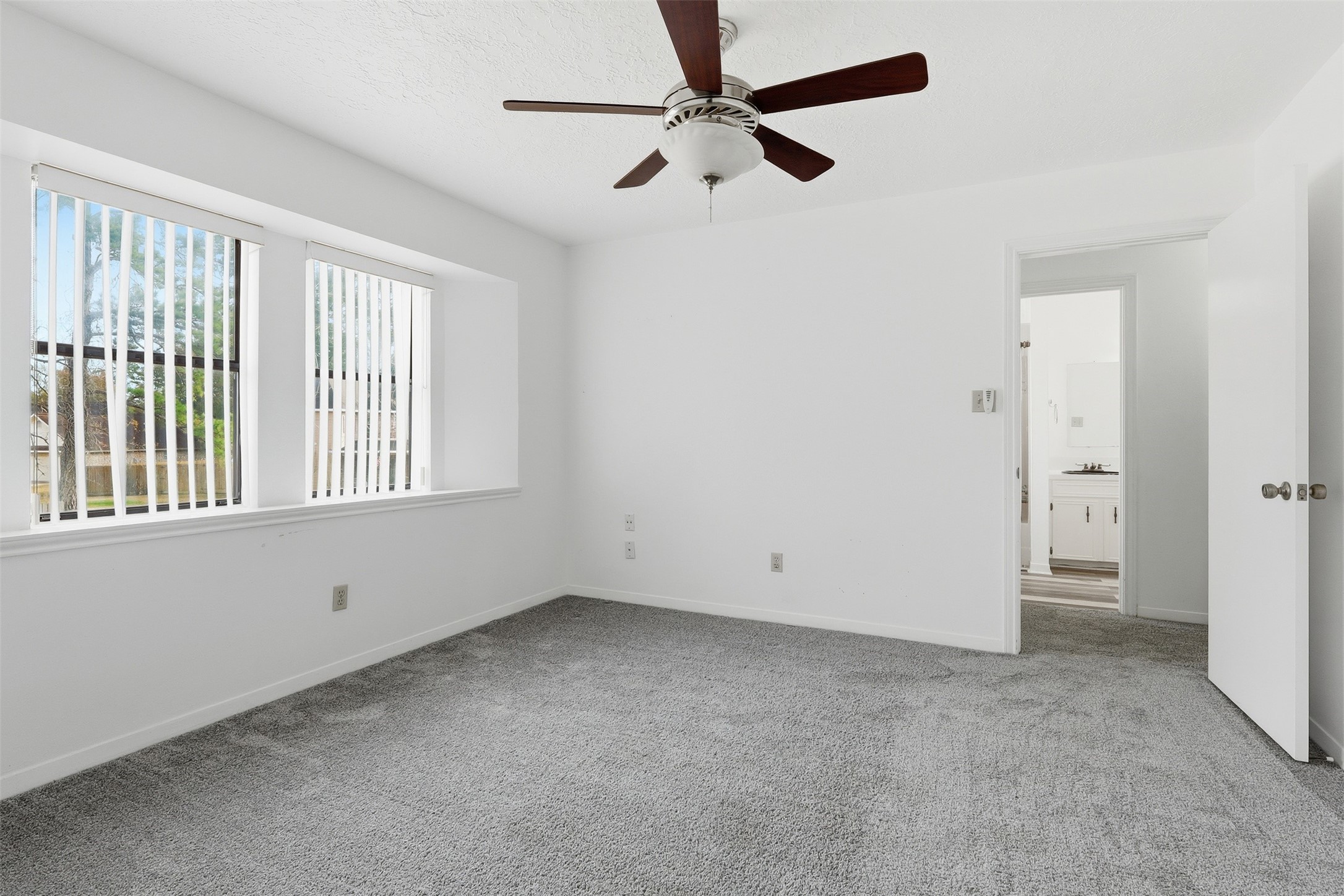 614 Tallow Drive Conroe, TX 77385 - Photo 26 of 36 Upstairs 2nd bedroom featuring a ceiling fan and large windows with vertical blinds. It includes an ensuite bathroom, enhancing convenience and privacy.