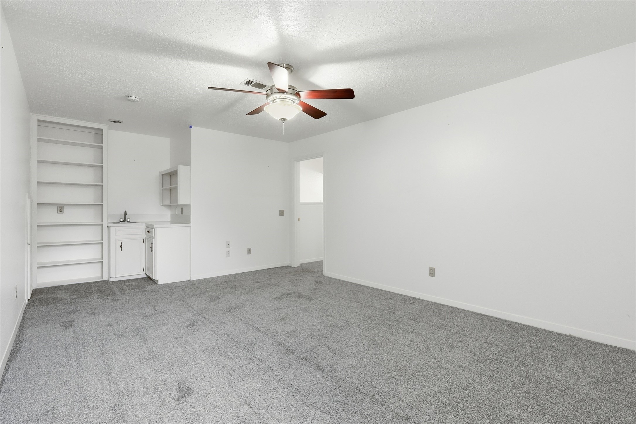614 Tallow Drive Conroe, TX 77385 - Photo 32 of 36 This bedroom features fresh gray carpeting, a ceiling fan, and a small built-in kitchenette with open shelving, perfect for a versatile living area or entertainment space.