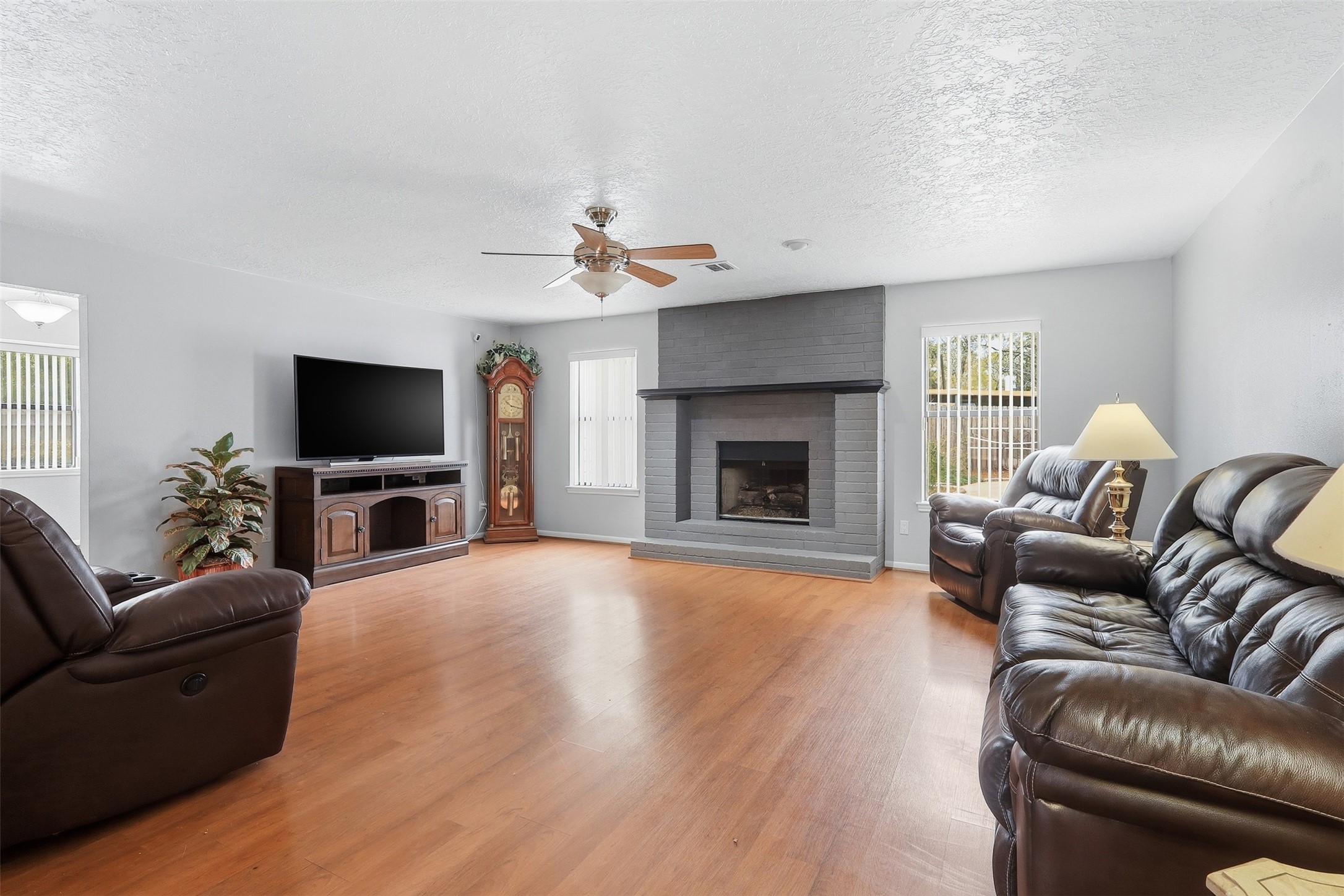 614 Tallow Drive Conroe, TX 77385 - Photo 6 of 36 This spacious living room features a cozy gray brick fireplace, large windows for natural light, and warm wood flooring. The room's layout is perfect for relaxation and entertaining.
