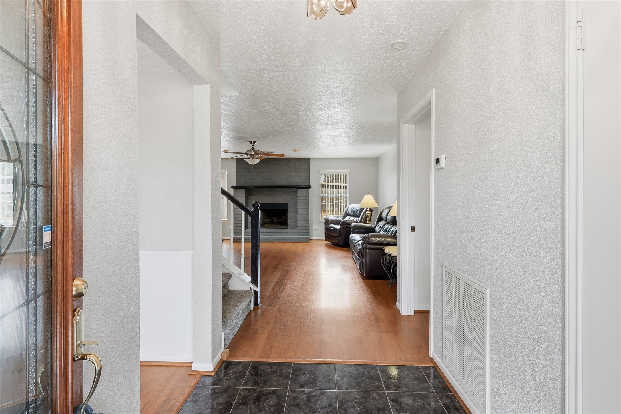 614 Tallow Drive Conroe, TX 77385 - Photo 9 of 36 This entryway leads to a cozy living room with wooden floors and a fireplace. It features neutral walls, a ceiling fan, and comfortable seating, creating a welcoming atmosphere.