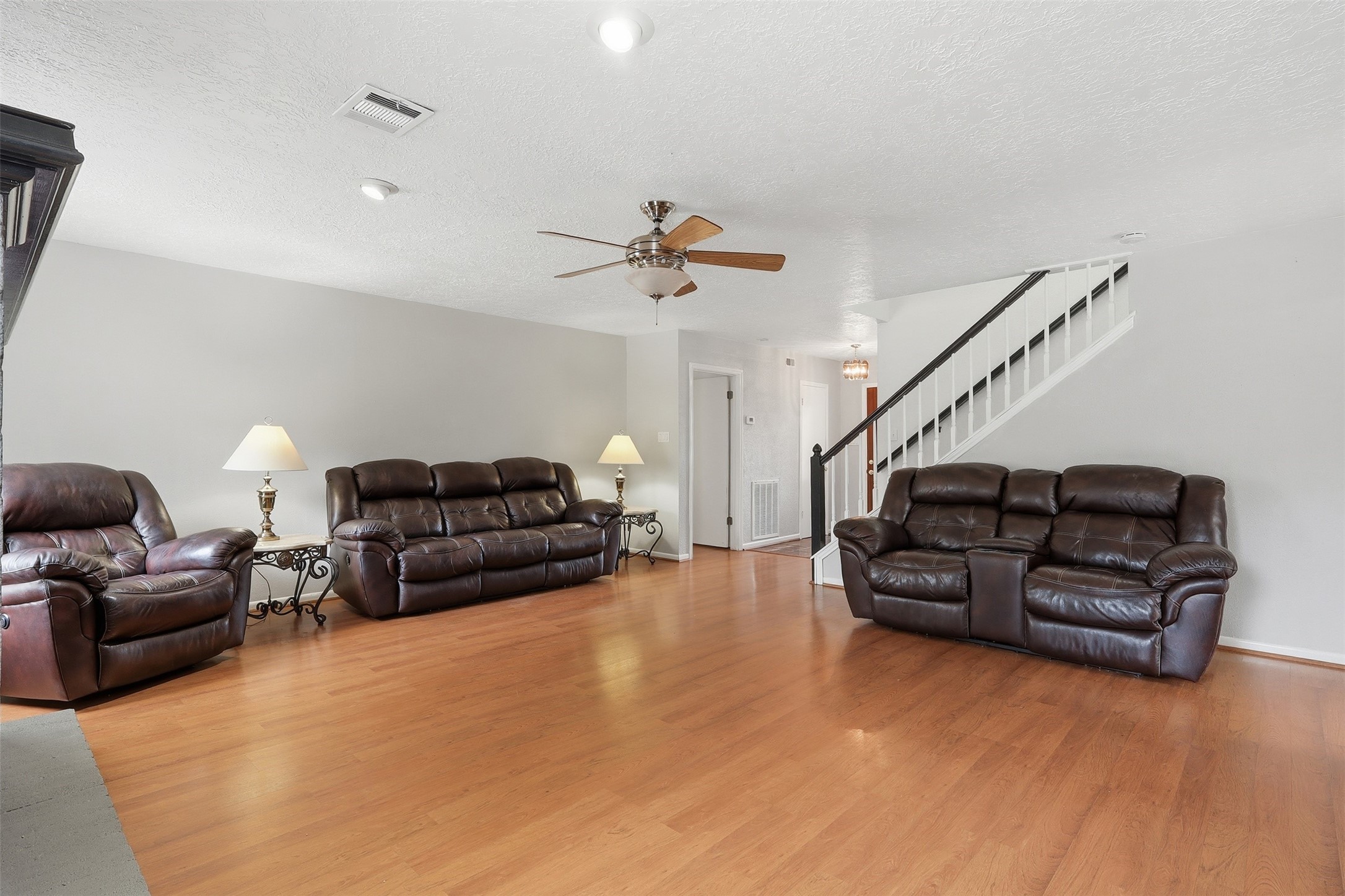 614 Tallow Drive Conroe, TX 77385 - Photo 10 of 36 Spacious living room with warm wood flooring, neutral walls, and ample light. Features comfortable leather seating, a ceiling fan, and an adjacent staircase. Ideal for relaxation and entertaining.