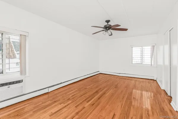 an empty room with wooden floor ceiling fan and windows