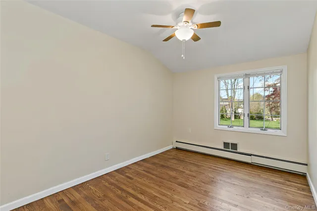 an empty room with wooden floor chandelier fan and windows
