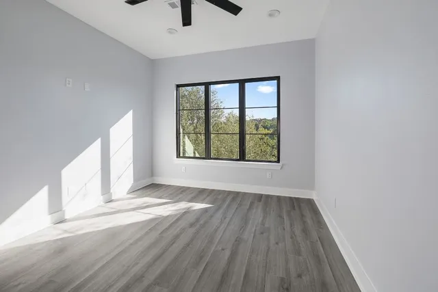 an empty room with wooden floor chandelier fan and windows