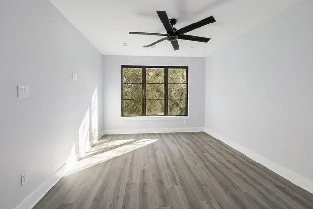 an empty room with wooden floor ceiling fan and windows