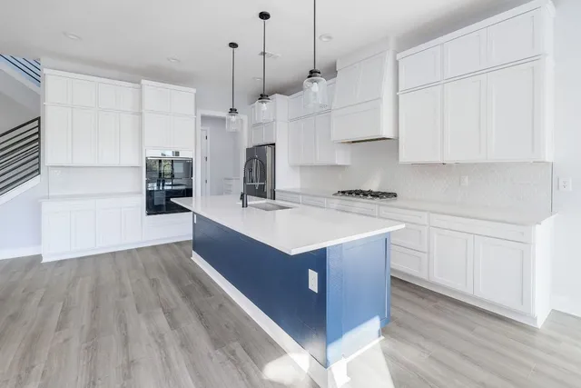 a kitchen with stainless steel appliances granite countertop a sink a stove a refrigerator and white cabinets with wooden floor