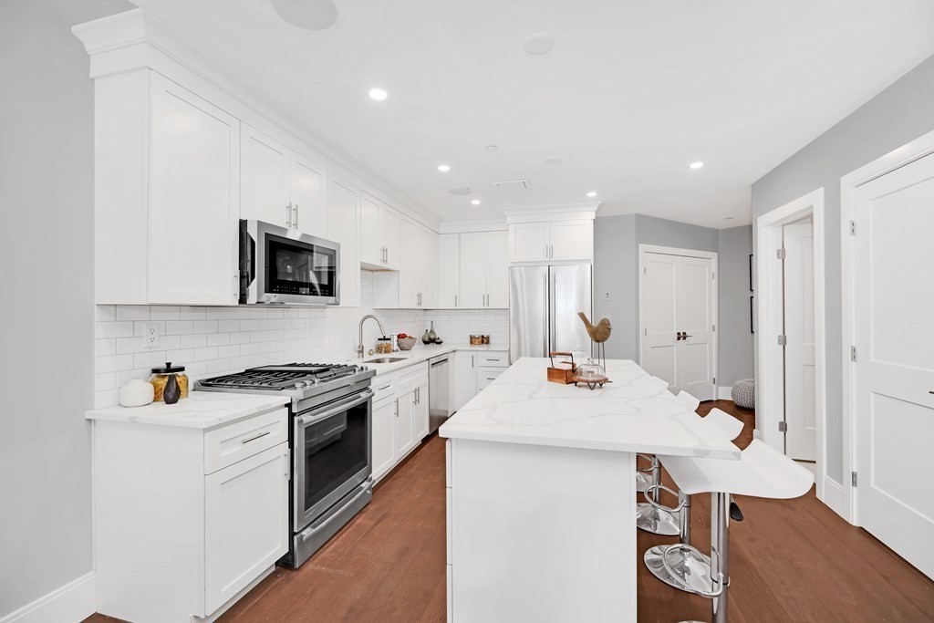 480 West Broadway, Unit 103 Boston, MA 02127 - Photo 5 of 19 a kitchen with a sink a stove cabinets and wooden floor