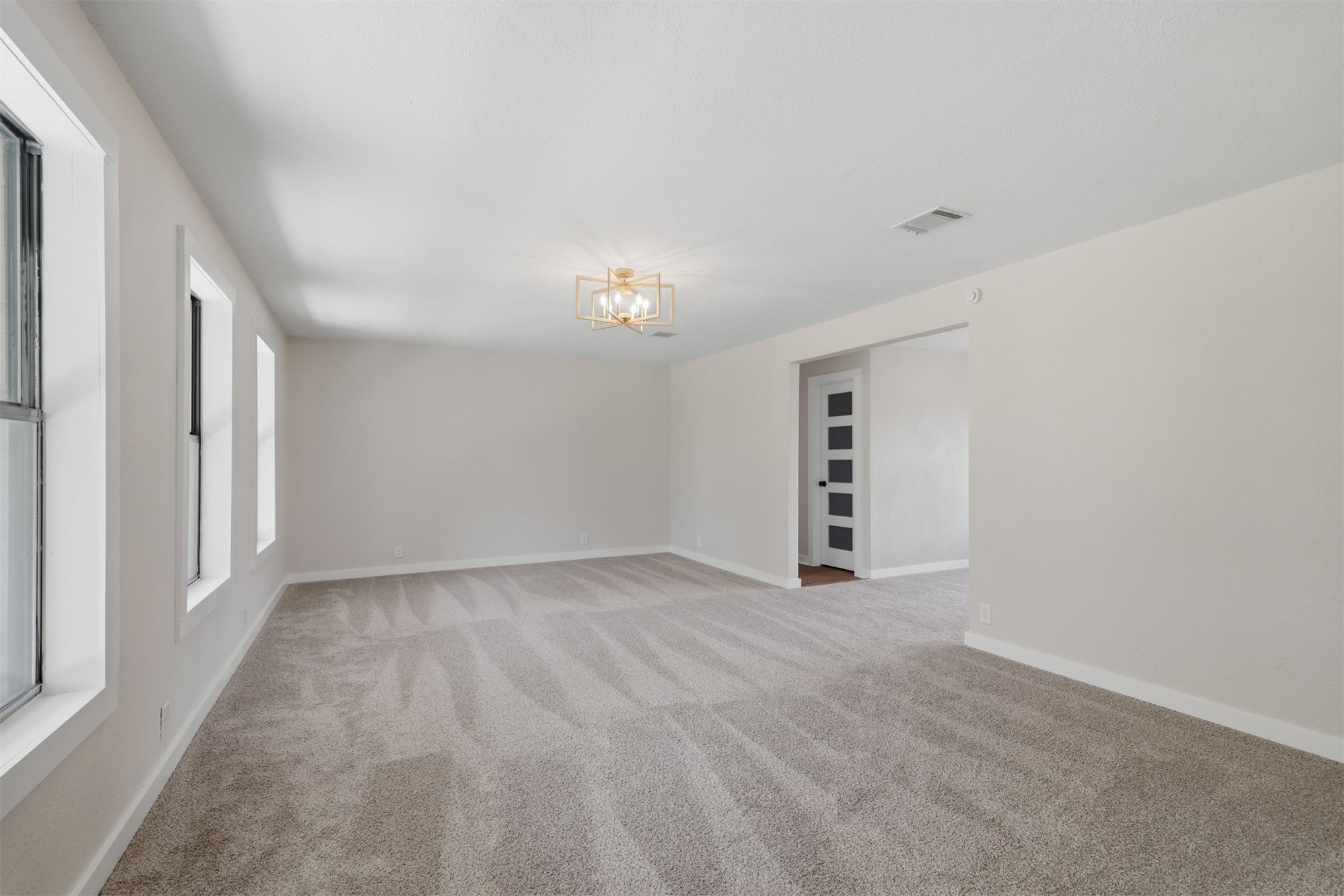 633 Swinney Road Mead, OK 73449 - Photo 9 of 32 Spacious room featuring light-toned carpeting, multiple windows with white trim, a modern ceiling light fixture, and a white interior door with frosted glass panels