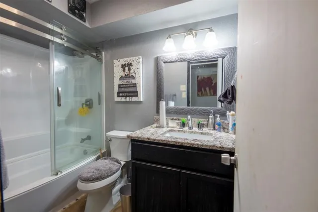 a bathroom with a granite countertop sink a toilet a mirror and shower