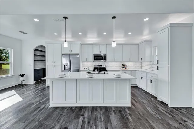 a large white kitchen with lots of counter space a sink appliances and cabinets